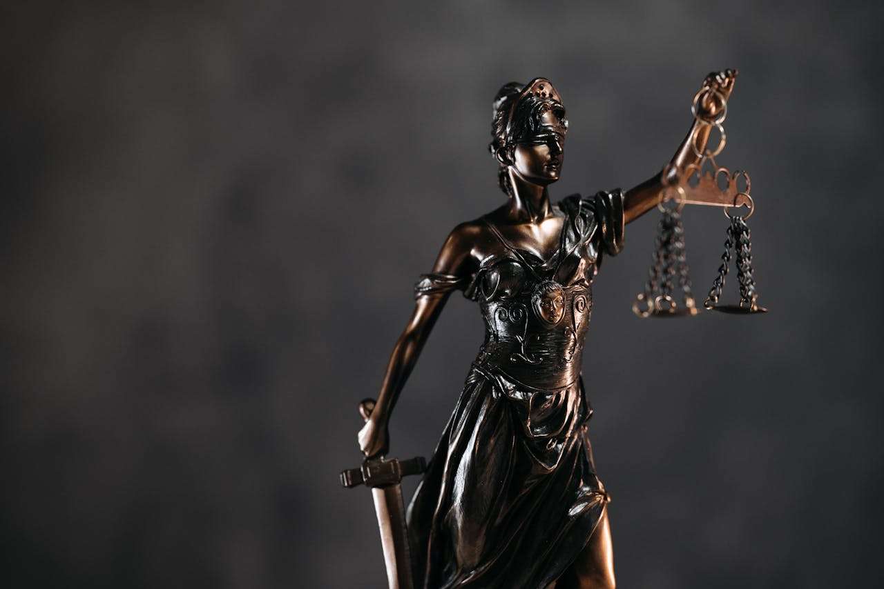 Detailed bronze Lady Justice statue with scales and sword against a dark background, symbolizing law and justice.